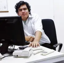 Persona sentada ante un monitor y un teléfono de escritorio.